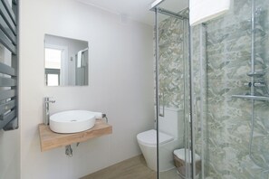 Et badeværelse med en hvid vask, toilet og et glasvægshus til brusebad.