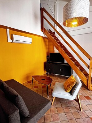 Een woonkamer met een bank, een salontafel, een stoel met kussen, een televisie, een kast en een trap.