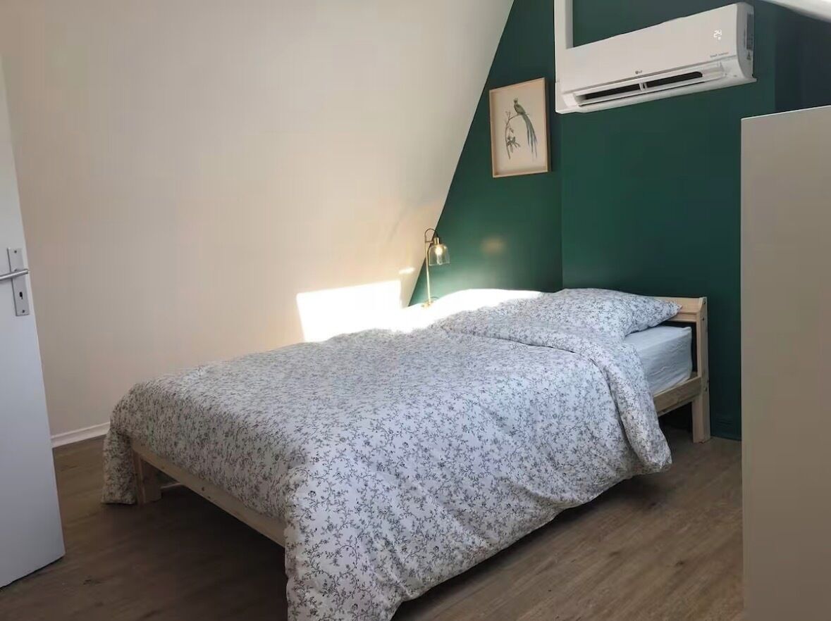 Ein Schlafzimmer mit einem Bett, einer Wand-Klimaanlage, einem gerahmten Bild und einer Nachttischlampe.