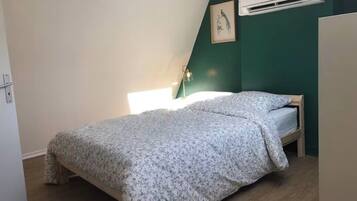Ein Schlafzimmer mit einem Bett, einer Wand-Klimaanlage, einem gerahmten Bild und einer Nachttischlampe.