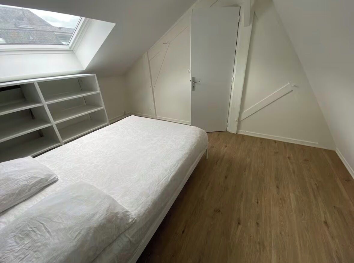 Ein Schlafzimmer mit Dachfenster, einem Bett, eingebauten Regalen, einem Kleiderschrank und Holzboden.