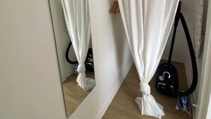 A room with a mirror, a white curtain, a vacuum cleaner, and a wooden floor.