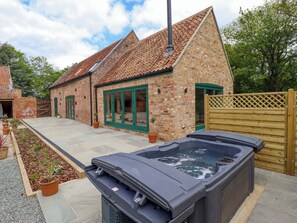 A brick building with a tiled roof, a wooden gate, and a hot tub in the foreground.