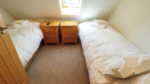Een slaapkamer met twee eenpersoonsbedden, een houten nachtkastje met lades, een afstandsbediening en een raam met uitzicht.