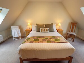 A bedroom with a bed, two bedside tables, a chair, a radiator, and a window. - Bobblehat Barn (Alford)