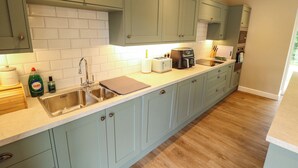 Een keuken met lichtgroene kastjes, witte metrotegels, een roestvrijstalen spoelbak, een broodrooster en een koffiezetapparaat.