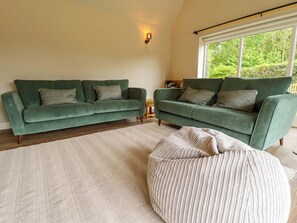 A living room with two green sofas, a beige rug, and a window with a view of greenery. - Bobblehat Barn (Alford)