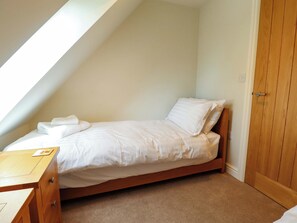 A single bed with a wooden frame, a wooden nightstand, and a door to the right.