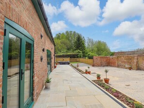 A brick building with a paved patio, potted plants, and a wooden fence. - Bobblehat Barn (Alford)