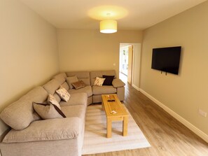 Ein Wohnzimmer mit einem Ecksofa, einem Couchtisch aus Holz und einem flachbildfernseher an der Wand.