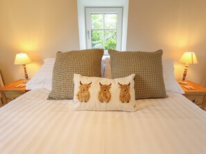 A bed with striped bedding, two matching pillows, a bedside lamp, and a window with a view of trees. - Bobblehat Barn (Alford)