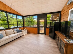 Ein modernes Interieur mit Holzboden, großen Fenstern, einer Couch, einem Fernseher und einem Kühlschrank.