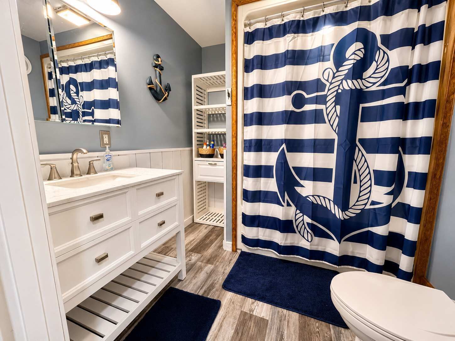 Une salle de bain avec un rideau de douche à rayures, un meuble-lavabo blanc, un miroir et un plancher en bois.