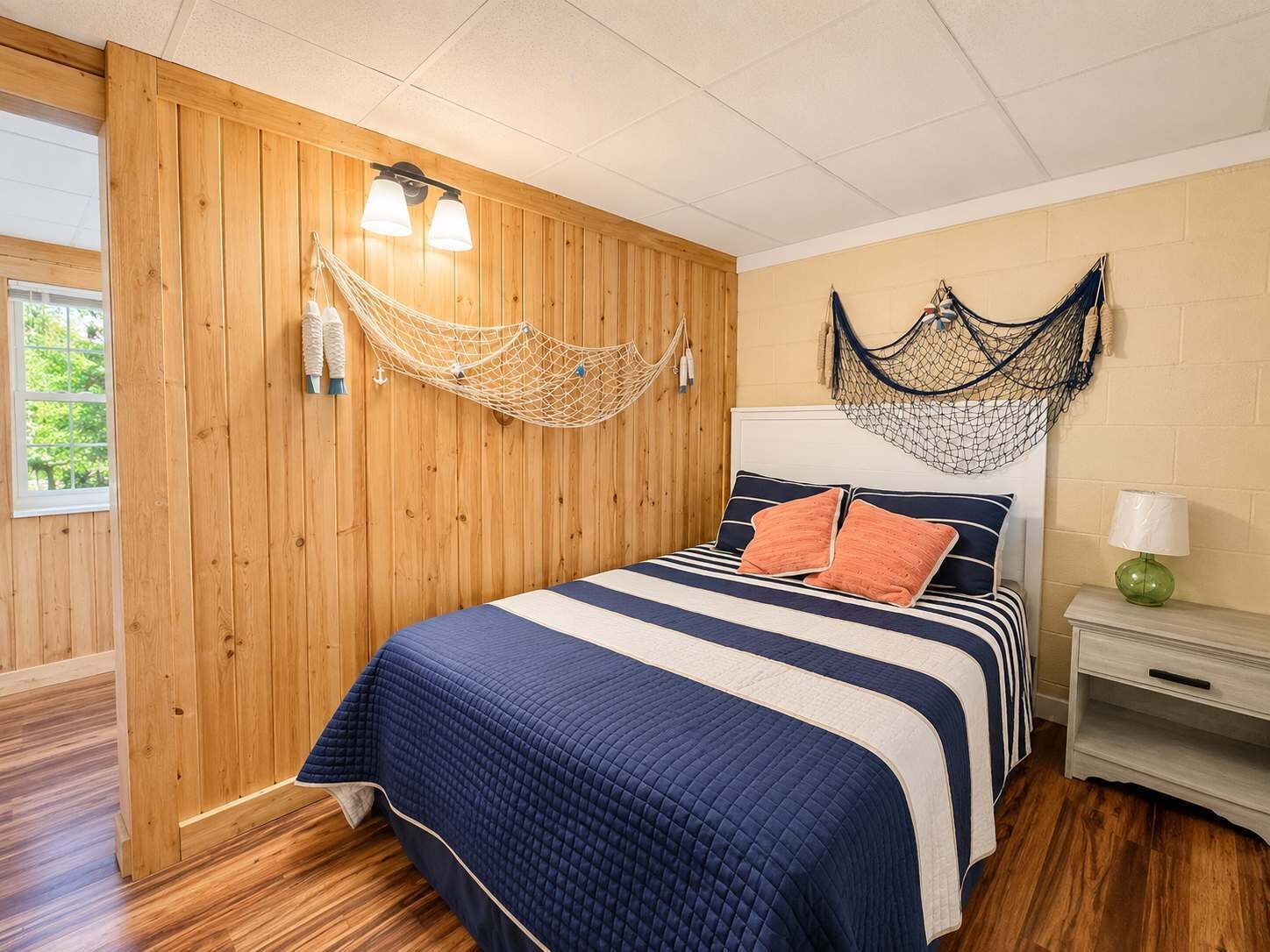 A room with a bed, wooden walls, a hammock, and a nightstand with a lamp.