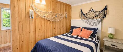 A room with a bed, wooden walls, a hammock, and a nightstand with a lamp.