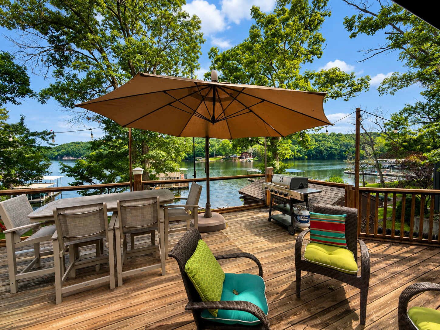 A deck with outdoor furniture, a grill, and a view of a lake.