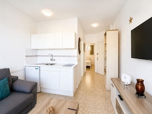 A compact living space with a kitchenette, a sofa, a TV, and a small table with a vase. - Ocean Views at Playa La Arena - Alma Homes (Puerto de Santiago)