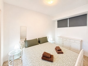 Ein Schlafzimmer mit einem Bett, einem Nachttisch, einer Lampe, einem Spiegel, einem Fenster und einem Kleiderschrank.