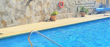 Una piscina con pared de piedra, un flotador salvavidas y plantas en macetas.