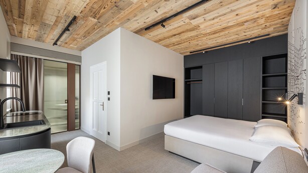 A modern bedroom with a wooden ceiling, a bed, a desk with a chair, and a built-in wardrobe. - Origin Prague (Prague)