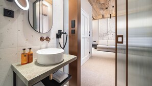 A modern bathroom with a round sink, a mirror with a light, and two bottles of shampoo. - Origin Prague (Prague)