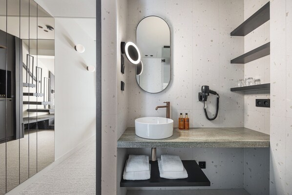 A modern bathroom with a round mirror, a sink, a hairdryer, and a towel rack. - Origin Prague (Prague)