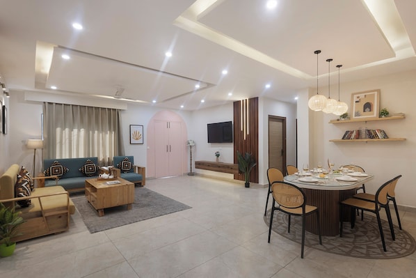 A modern living room with a sofa, coffee table, and dining table set for six. - Alaya Stays Snowdrop 3 BHK Apartment (Mussoorie)