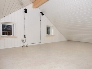 Quarto com paredes brancas, painéis, duas janelas e teto inclinado.