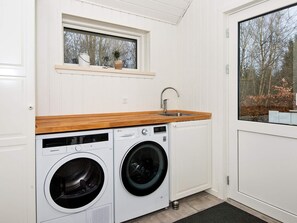 Ein Waschraum mit zwei Waschmaschinen, einer Holzauskładung, einem Waschbecken und einem Fenster mit Blick auf Bäume.