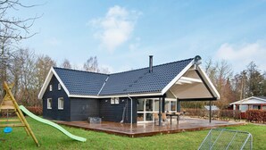 A modern house with a large deck, a play area with a slide, and a fenced yard. - 4 Star Holiday Home in Silkeborg (Silkeborg)