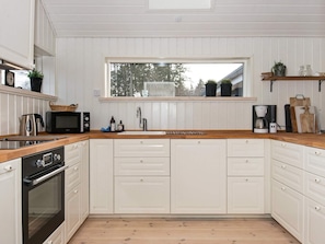 A kitchen with white cabinetry, a wooden countertop, a built-in oven, a coffee maker, and a window with a view of trees. - 4 Star Holiday Home in Silkeborg (Silkeborg)
