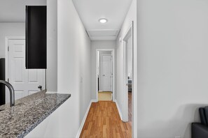 A hallway with a kitchen counter, wooden flooring, white walls, and a door at the end. - King George 2BR Luxury Stay (Savannah)