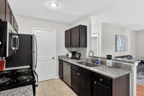 A modern kitchen with a granite countertop, black cabinets, a built-in oven, and a coffee maker. - King George 2BR Luxury Stay (Savannah)