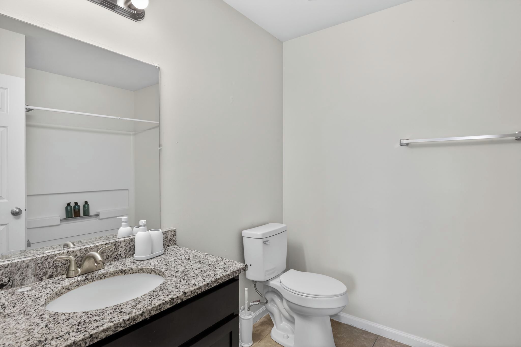 A bathroom with a granite countertop sink, a white toilet, a mirror, and a towel rack.