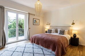 Ein Schlafzimmer mit großem Fenster, einer Kristallleuchter, einem Bett mit gemustertem Überwurf, zwei Nachttischlampen und einem Teppich.