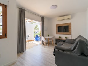 Ein modernes Wohnzimmer mit einer Couch, einem an der Wand befestigten Fernseher, einem Esstisch mit Stühlen und einem großen Fenster mit Vorhängen.