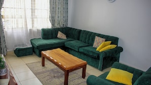 Una sala de estar con un sofá verde, una mesa de centro de madera y un reloj en la pared.