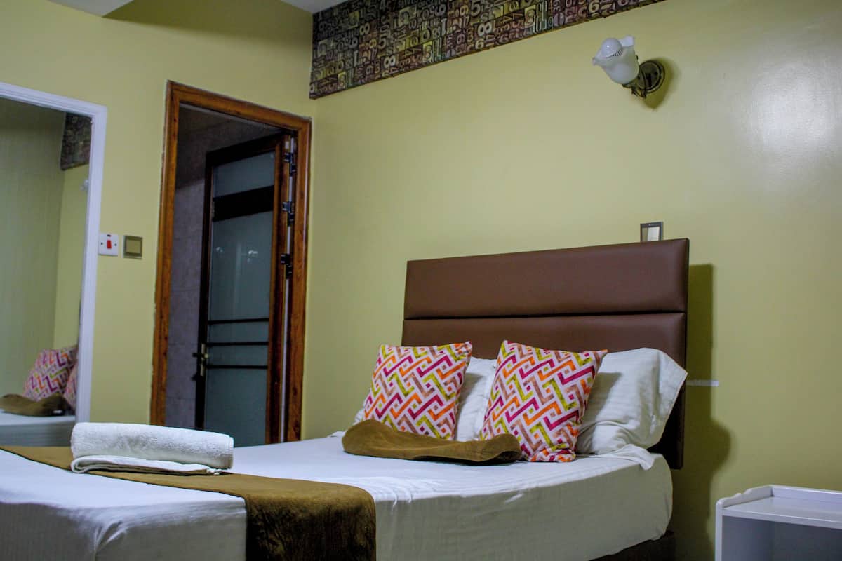 Una habitación de hotel con una cama, una mesita de noche, un espejo y una puerta.