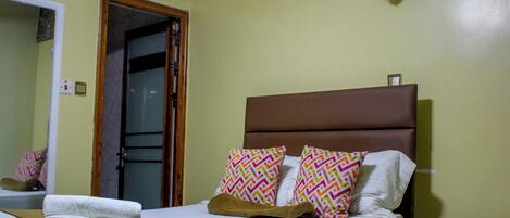 A hotel room with a bed, a bedside table, a nightstand, a mirror, and a door.