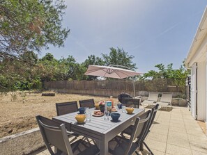 Eine Terrasse im Freien mit einem Essplatz, umgeben von Stühlen und einem großen Sonnenschirm.