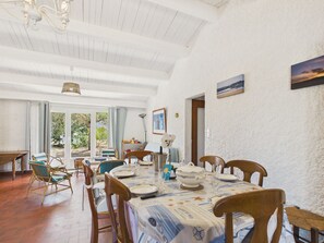 Ein Essbereich mit einem Tisch für vier Personen, Holzstühle, einer Chandelüster und Blick ins Freie.