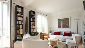 Un salon spacieux avec un canapé blanc, une table basse et une bibliothèque remplie de livres.