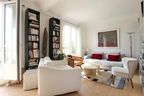 A spacious living room with a white sofa, a coffee table, and a bookshelf filled with books. - Stunning flat with terrasse - Trocadéro (Paris)