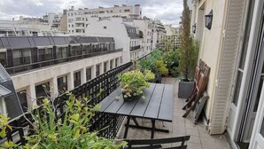 Une terrasse sur le toit, avec une table et des chaises, entourée de plantes en pot et offrant une vue sur le paysage urbain.