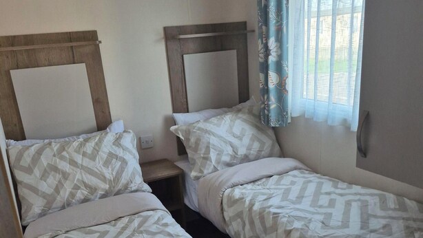A twin room with two beds, a nightstand, and a window with curtains.