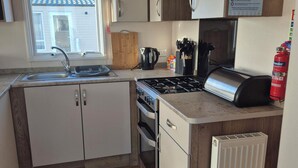 A compact kitchen with a gas stove, sink, and a window overlooking a house.