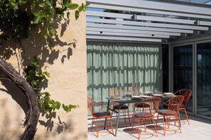 Un espace repas comprenant une table et des chaises, une pergola et une vue à travers une porte vitrée.