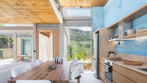 A modern kitchen with a wooden table and white chairs, a built-in oven, and a view of greenery outside. - Anassa House with Rooftop Jacuzzi (Apokoronas)