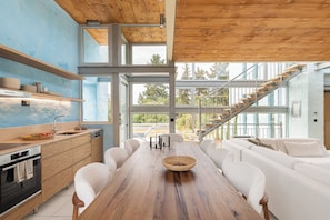 A modern kitchen with wooden cabinetry, a dining table with white chairs, and a staircase leading to an upper level.