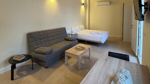 A modern room with a sofa, a bed, a small table, and a TV mounted on the wall. - La Corte de Isabel (Cordoba)